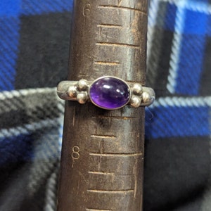 Puede incluir: Un anillo de plata con una piedra preciosa de amatista púrpura y pequeñas cuentas de plata en la banda.