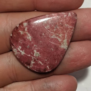 Peut inclure: Une pierre précieuse en forme de larme, rose et blanche, avec une surface lisse et polie.