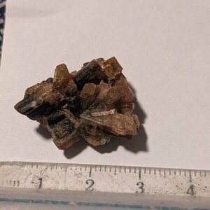 May include: A cluster of brown and green crystals with a slightly pink hue. The crystals are about 2 inches in diameter.