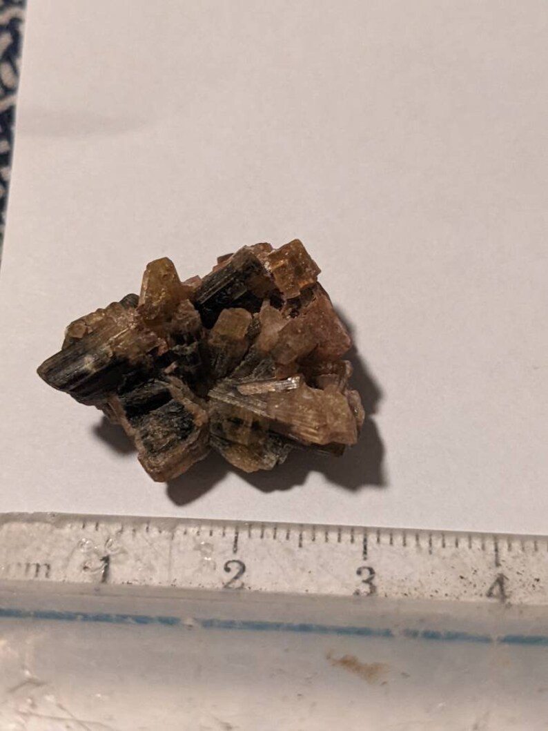 May include: A cluster of brown and green crystals with a slightly pink hue. The crystals are about 2 inches in diameter.