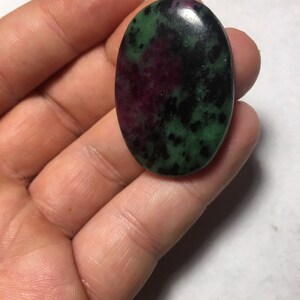 May include: Oval shaped green, black, and pink gemstone cabochon.