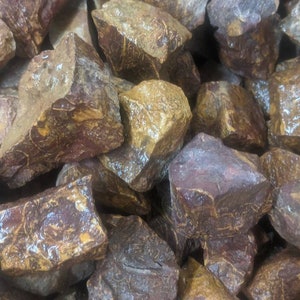 May include: A close-up of a pile of red and brown stones with yellow and white markings. The stones are rough and have an irregular shape.