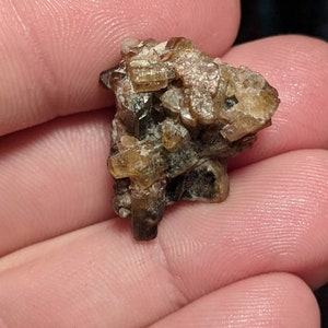 May include: A cluster of brown and gold crystals with a rough, natural texture. The crystals are clustered together in a random, organic shape.