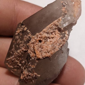 May include: A clear quartz crystal with a brown and orange matrix. The crystal is double terminated and has a natural, rough texture.