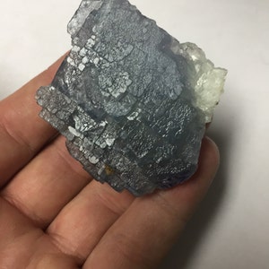 May include: A blue fluorite crystal with a white, translucent section. The crystal has a layered, geometric structure and a rough, textured surface.