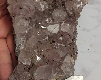 May include: A cluster of amethyst crystals with a light purple hue. The crystals are arranged in a natural formation and have a smooth, glassy surface. The cluster is approximately 4 inches wide.