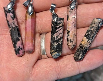 May include: Five pink and black gemstone pendants with silver bail settings. The pendants are all different shapes and sizes, but they are all polished and have a smooth finish.
