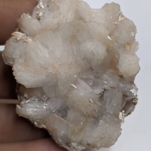 May include: A cluster of white, translucent crystals with a rough, natural texture. The crystals are arranged in a dense, layered formation, creating a visually interesting and unique specimen.