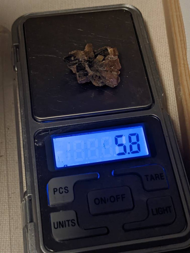 May include: A small, brown and black crystal cluster is weighed on a digital scale. The scale reads 5.8 grams.