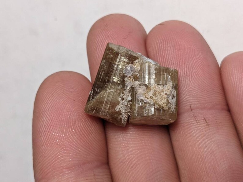 Może przedstawiać: Brązowy i biały kryształ o powierzchni prążkowanej. Kryształ ma około 5 cm długości i 2,5 cm szerokości.