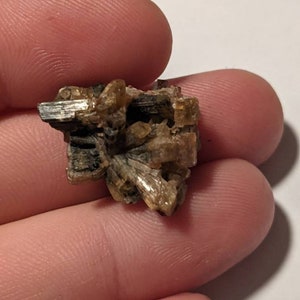 May include: A cluster of small, brown, and gold crystals. The crystals are arranged in a random pattern and have a rough, textured surface.