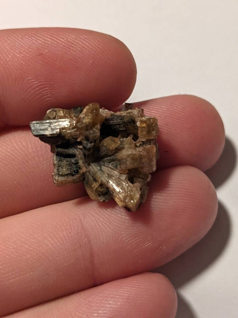 May include: A cluster of small, brown, and gold crystals. The crystals are arranged in a random pattern and have a rough, textured surface.