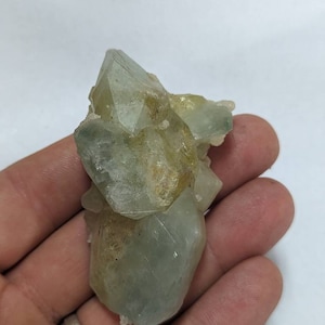 May include: A cluster of light green and yellow crystals with a clear, glassy appearance. The crystals are clustered together in a rough, natural formation.