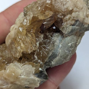 May include: A close-up of a rock with a large, clear, crystalline formation inside. The crystals are a light brown colour and have a rough, textured surface.
