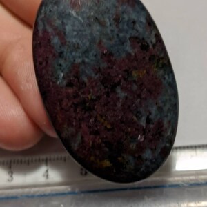 Può includere: Una pietra liscia di forma ovale lucidata con un motivo a spirale di blu scuro, viola e oro. La pietra è lunga circa 7,5 cm.