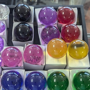 May include: A collection of colorful glass marbles in various colors, including purple, red, yellow, green, and blue. Some of the marbles have writing on them, including "Made in China" and "740".