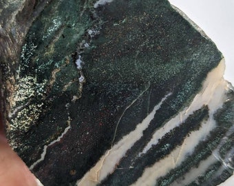 May include: A slab of green, black and white banded agate with a rough, natural surface.