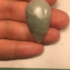 以下が含まれることがあります： 滑らかで磨かれた表面を持つ、涙滴型の薄い緑色の宝石のカボションです。