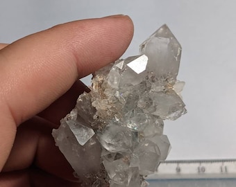 May include: A cluster of clear quartz crystals with a slightly cloudy appearance. The crystals are clustered together in a natural formation, with some smaller crystals surrounding the larger ones. The crystals have a slight iridescent sheen.