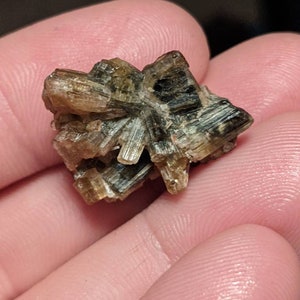 May include: A cluster of brown and green crystals with a starburst shape.