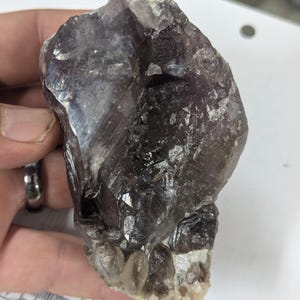 May include: A large, dark purple amethyst crystal with a smoky quartz base. The crystal has a rough, natural texture and is translucent.
