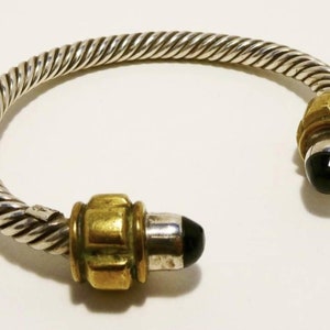 May include: A silver and gold bangle bracelet with a twisted design and black onyx stones on each end.