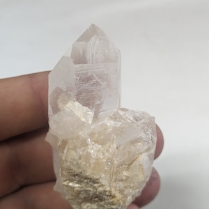 May include: A clear quartz crystal cluster with a large, pointed crystal on top. The cluster is surrounded by smaller, clear crystals and has a rough, natural texture.