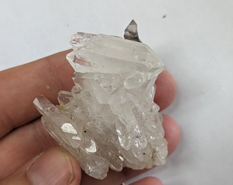 May include: A cluster of clear quartz crystals with a pointed tip, forming a natural crystal formation.
