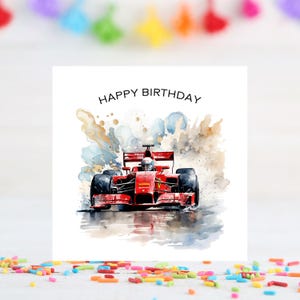 May include: A birthday card featuring a red race car in a watercolor style. The card has the words "HAPPY BIRTHDAY" at the top. The background has blue, gold, and gray watercolor splashes.