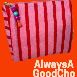 May include: A rectangular zippered pouch made of pink and red striped terry cloth fabric. The zipper pull features two purple beads, one light blue bead, and a small orange tassel. Text reads PINK! PINK! PINK! PINK! PINK! and AlwaysA GoodChoice.