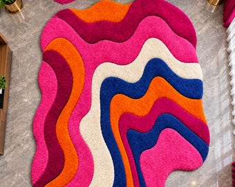 May include: An irregular rectangle rug featuring a high-pile texture with a vibrant, wavy pattern. The design consists of flowing, organic bands in shades of bright pink, deep magenta, vivid orange, royal blue, and cream, creating a bold visual.