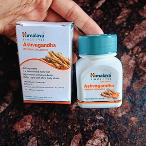 May include: A white box and bottle of Himalaya Ashvagandha tablets. The box and bottle have the text "Ashvagandha General Wellness" and "Pure Herbs". The box shows an illustration of the herb. The bottle contains 60 tablets.