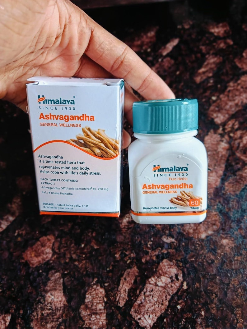 May include: A white box and bottle of Himalaya Ashvagandha tablets. The box and bottle have the text "Ashvagandha General Wellness" and "Pure Herbs". The box shows an illustration of the herb. The bottle contains 60 tablets.
