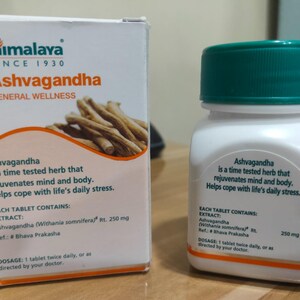 May include: A white box and bottle of Himalaya Ashvagandha supplements. The box features the brand logo and text, along with an illustration of the herb. The bottle has a green cap and white label with product information.