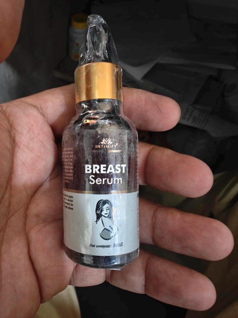 Puede incluir: Una peque&ntilde;a botella oscura de Suero para Senos Intimify con tapa dorada. La etiqueta presenta el nombre del producto y una ilustraci&oacute;n de una mujer. La botella contiene 30 ml de suero.