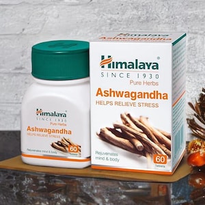 May include: A white bottle and box of Himalaya Ashwagandha tablets. The bottle has a green cap and the box displays the text "Helps Relieve Stress". The image shows the product on a wooden surface.