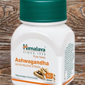 May include: A white bottle of Himalaya Ashwagandha tablets with a green cap. The label includes the text "Ashwagandha HELPS RELIEVE STRESS" and "60 Tablets". The background is a wooden surface.