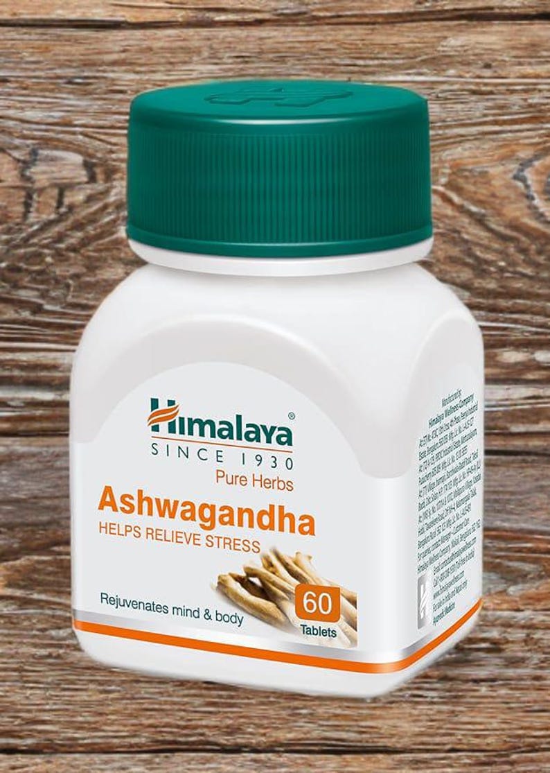 May include: A white bottle of Himalaya Ashwagandha tablets with a green cap. The label includes the text "Ashwagandha HELPS RELIEVE STRESS" and "60 Tablets". The background is a wooden surface.