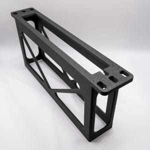 May include: A matte black, rectangular, 3D-printed frame with a hollow center and diagonal support struts. The top edge features three distinct rectangular cutouts on one end, while the overall structure exhibits a rigid, open-grid design.