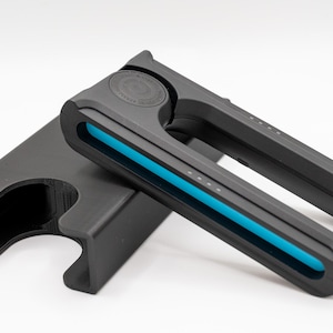 May include: A black hair styling tool with a bright blue accent, resting on a black stand. The tool has a curved design with a series of small white dots and a circular emblem. The stand has a unique shape with a curved opening.