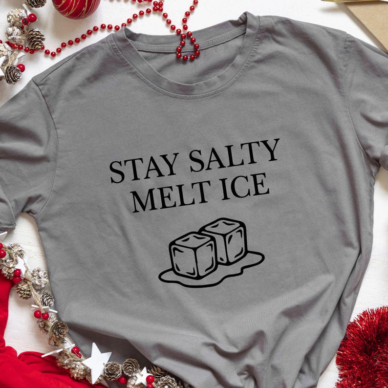 May include: A gray t-shirt with the text "STAY SALTY MELT ICE" in black, along with a graphic of two melting ice cubes. The shirt is a casual wear item.