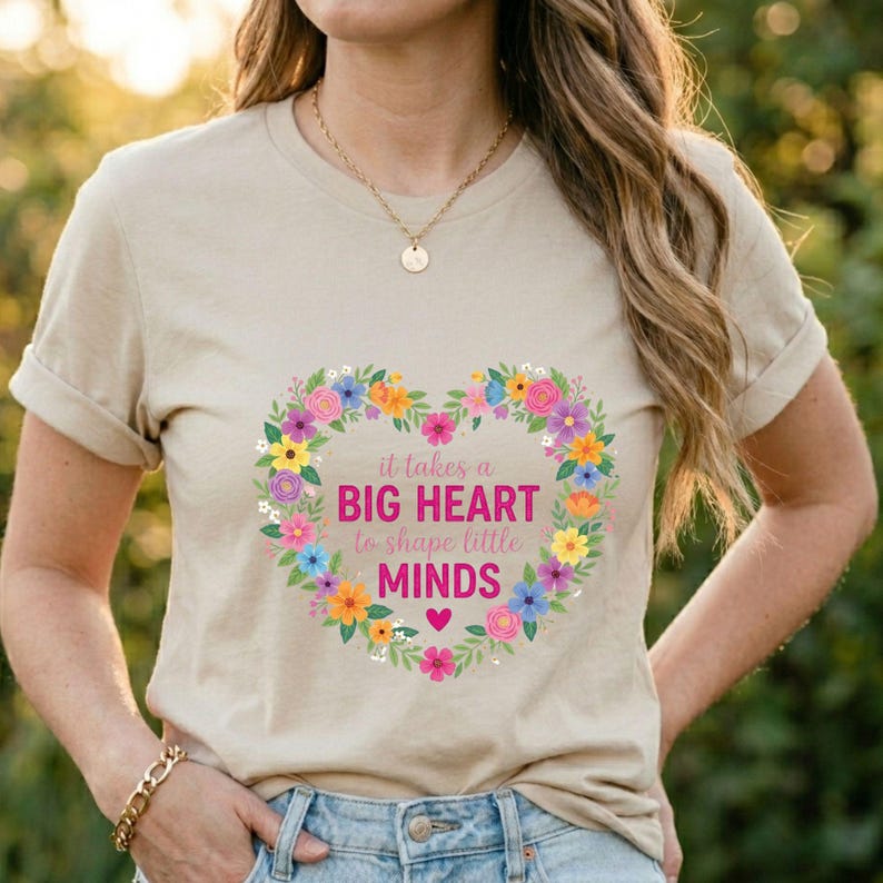May include: Beige t-shirt with a floral heart design. The heart is composed of colorful flowers and contains the text "it takes a BIG HEART to shape little MINDS". A gold necklace and bracelet are also visible.