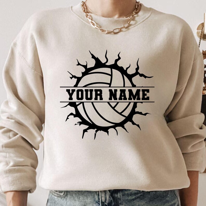Op de afbeelding: Beige sweatshirt met een zwarte volleybalafbeelding. Het volleybalontwerp is omgeven door een gekarteld barsteffect, met de tekst "YOUR NAME" in een vetgedrukte, blokletter. De sweatshirt heeft een ronde hals en lange mouwen.