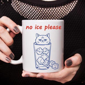 May include: White ceramic mug with the phrase "no ice please" in red lettering. A blue illustration depicts a grumpy cat in a glass filled with ice cubes. The mug has a white handle.