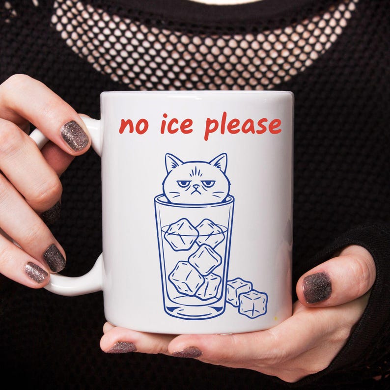 May include: White ceramic mug with the phrase "no ice please" in red lettering. A blue illustration depicts a grumpy cat in a glass filled with ice cubes. The mug has a white handle.