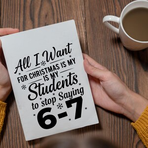 May include: A white rectangular sign held by a person, with the text "All I Want For Christmas Is My Students to stop Saying 6-7" in black script. The sign is decorated with snowflakes.