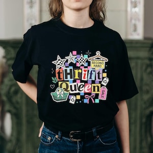 Może przedstawiać: Czarny t-shirt z kolorowym wzorem graficznym. Projekt zawiera słowa "Thrift Queen" w stylu kolażu, a także gwiazdy, wieszak, koszyk na zakupy oraz słowa "Second Hand" i "Sale".