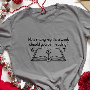 May include: A gray t-shirt with the text "How many nights a week should you be reading?" above a graphic of an open book with a heart. The numbers 6 and 7 are on either side of the book.