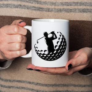 May include: A white ceramic mug with a black handle and the text "But First, Coffee" in a bold, black font. The mug is set against a blurred background, highlighting its clean design.