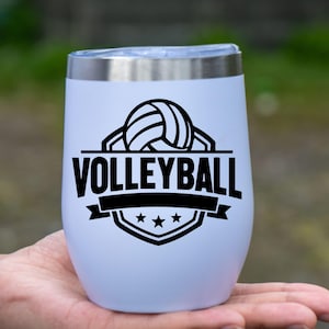 Op de afbeelding: Een witte ge&iuml;soleerde tumbler met een zilveren rand, met een zwarte volleybalafbeelding en het woord "VOLLEYBALL". Het ontwerp bevat een volleybal, banner en sterren.